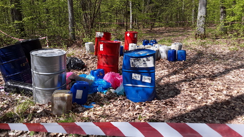 Beczki i kanistry o różnej pojemności z odpadami nielegalnie zgromadzone na otwartym terenie.