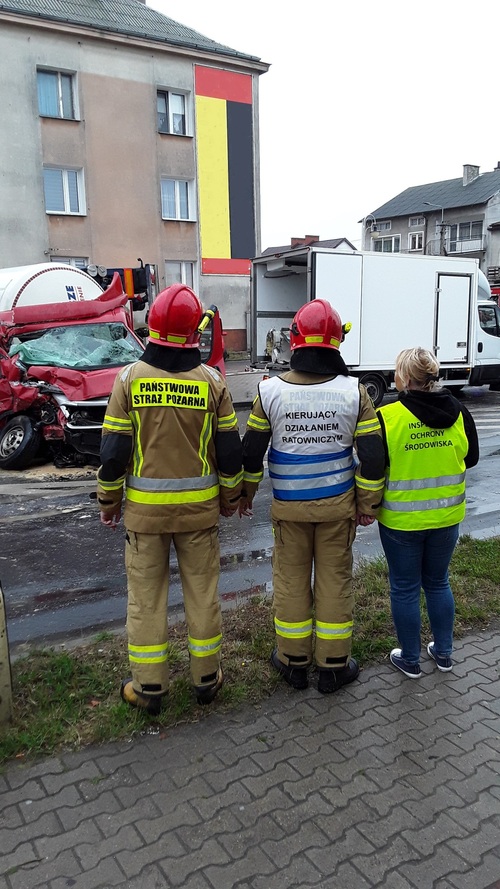 Inspektor Wojewódzkiego Inspektoratu Ochrony Środowiska w Warszawie i dwóch funkcjonariuszy Straży Pożarnej obserwują miejsce kolizji cysterny i auta dostawczego.