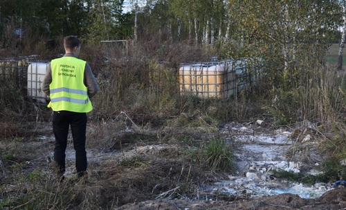 Inspektor Wojewódzkiego Inspektoratu Ochrony Środowiska w Warszawie stoi przed porzuconymi na zarośniętym terenie kilkoma zbiornikami o pojemności 1000 l.